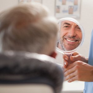Man smiling while looking at reflection in handheld mirror