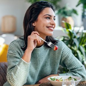 Woman in green sweater eating salad at home