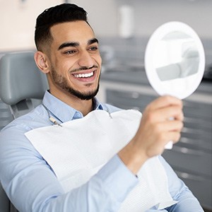 Man smiling at reflection in handheld mirror