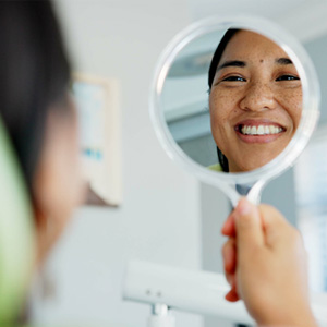 Individual smiling in the mirror at the dentist’s office 