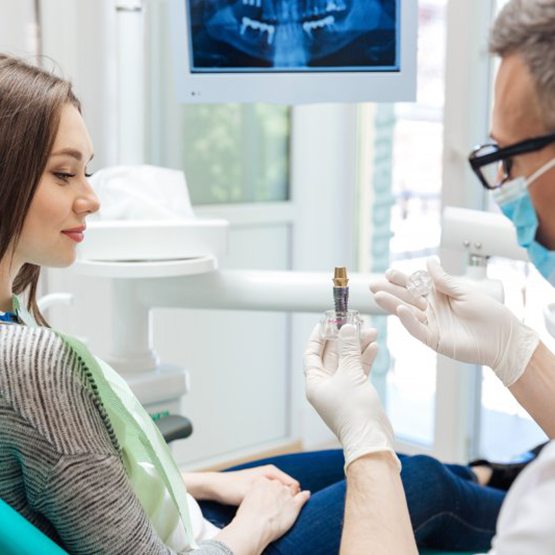 Dentist showing a patient a dental implant model 