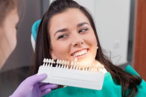 Young woman smiling with veneer models held up to her teeth.