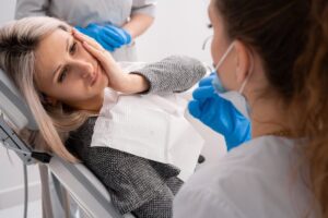Woman holding face in pain in dentist's chair.